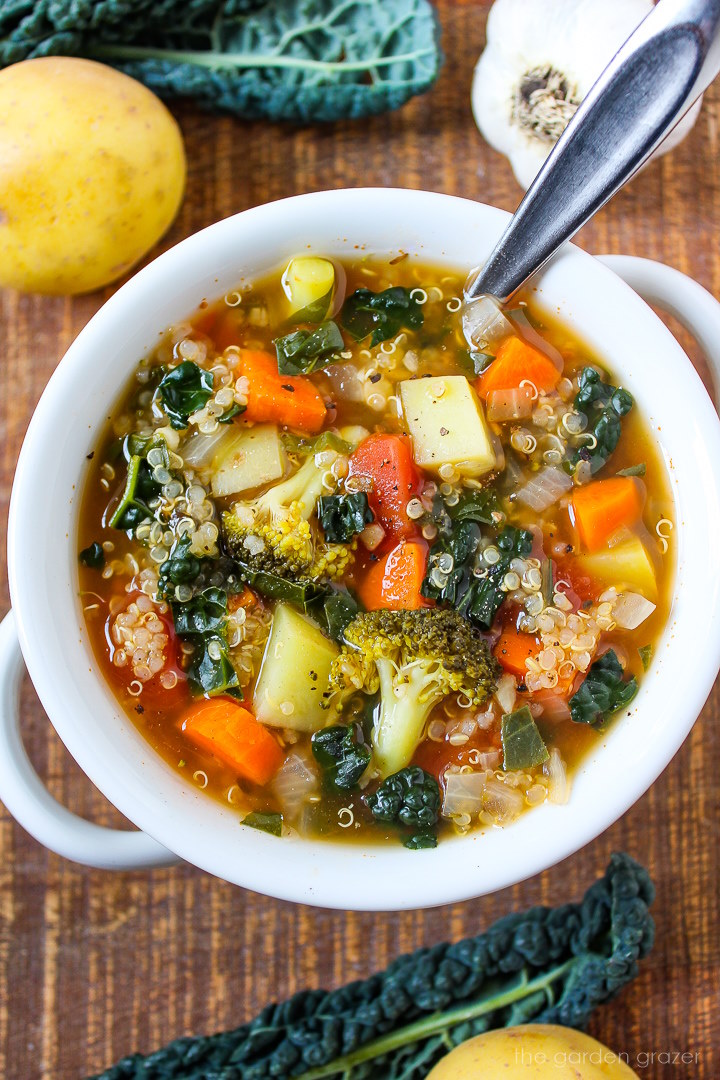 Quinoa potato soup in a white serving bowl with spoon on a wooden table
