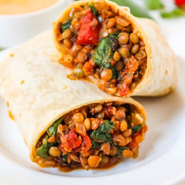 Lentil spinach burritos cut in half served on a white plate