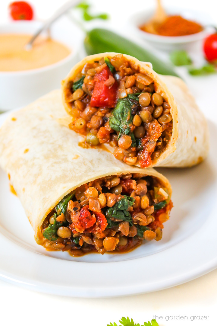 Lentil spinach burritos cut in half served on a white plate