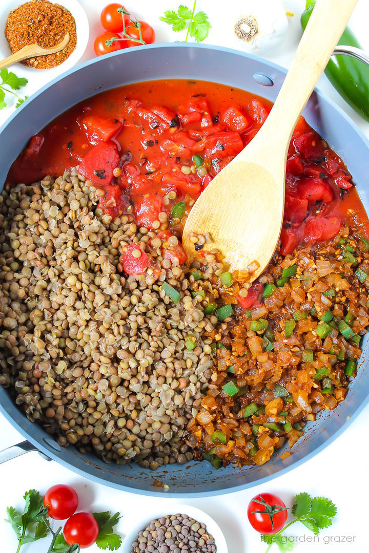 Overhead view of preparing lentil burrito mixture in a large pan with wooden spoon