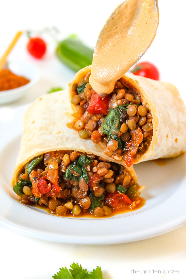 Spooning chipotle crema sauce over lentil burritos on a white place