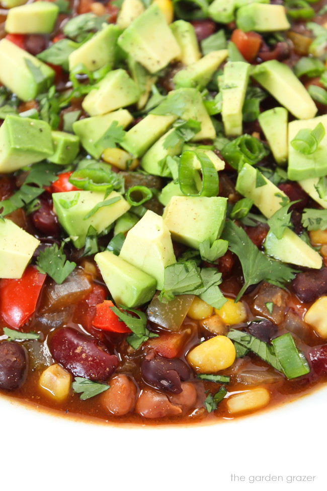 Close up view of bean chili in a white bowl topped with avocado