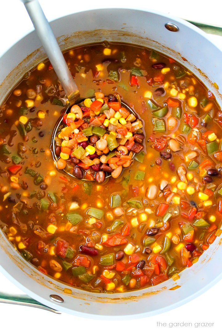 Overhead view of vegan three bean chili cooking in a large pot with soup ladle