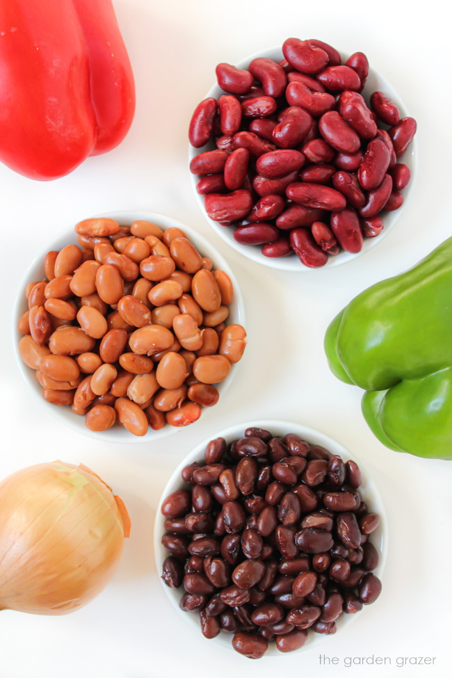 Ingredients such as beans, bell peppers, and onions on a white table