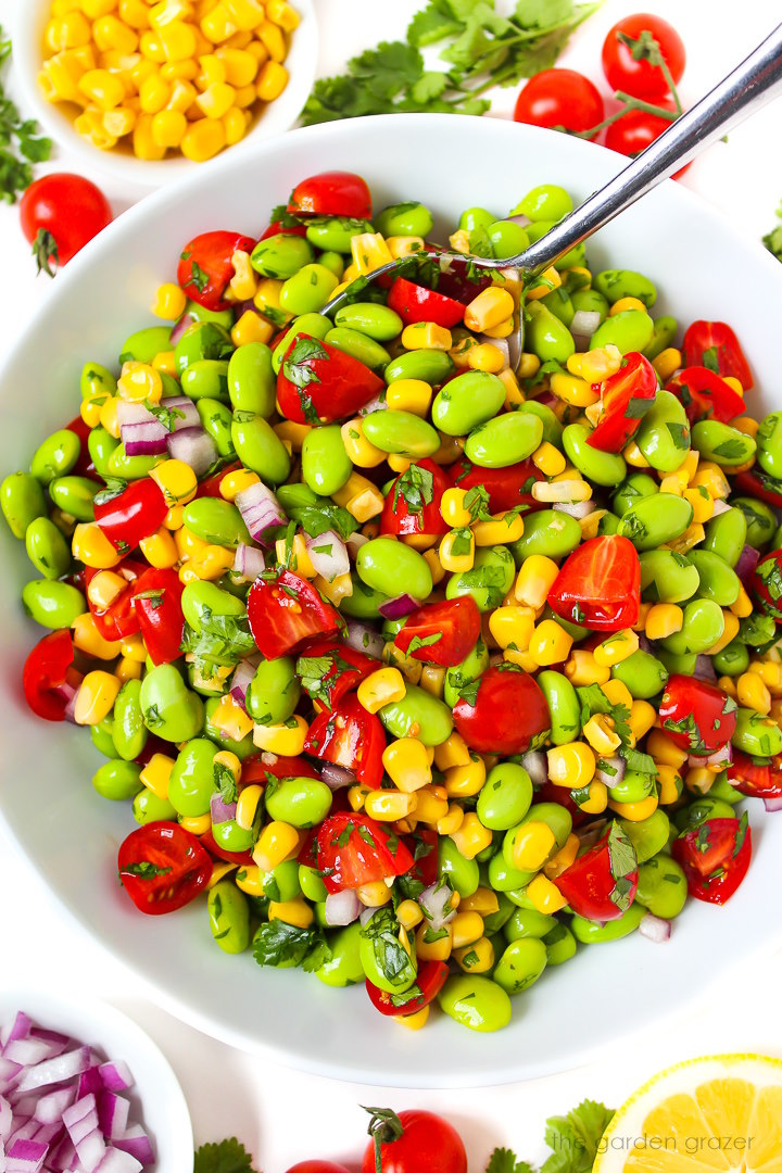 Overhead view of edamame corn salad with lemon in a white serving bowl