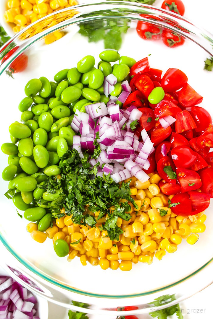 Overhead view of preparing salad ingredients in a large glass bowl before mixing together
