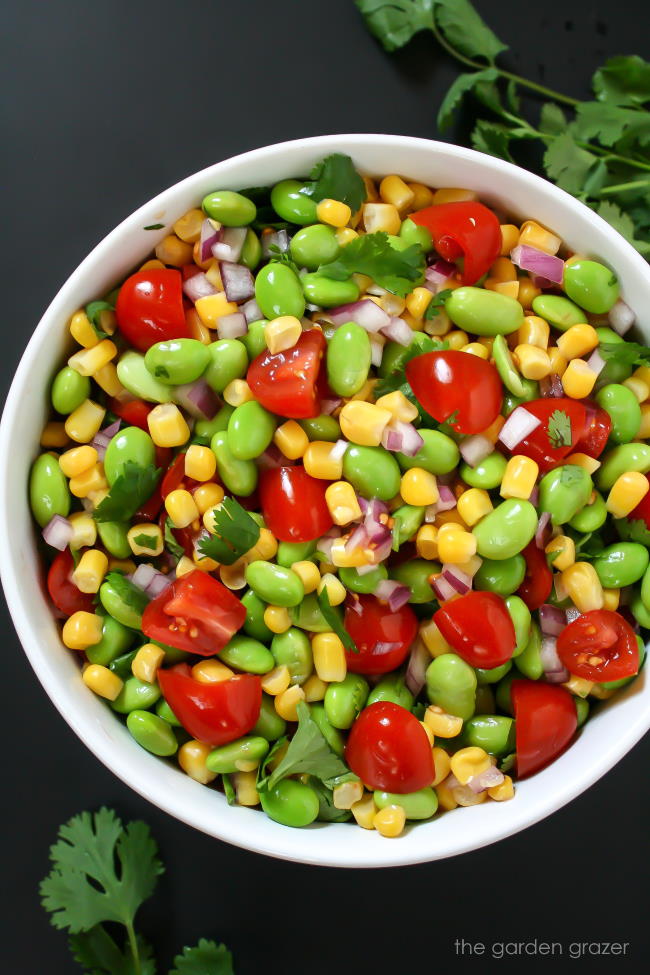 Lemony edamame corn salad tossed together in a bowl with tomato and cilantro