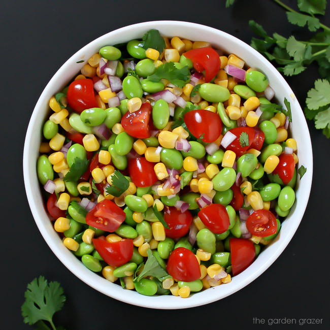 Lemony edamame corn salad tossed together in a bowl with tomato and cilantro