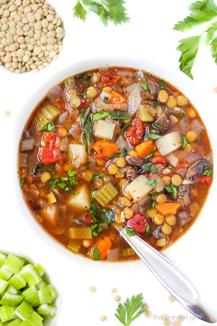 Vegan lentil vegetable soup in a white bowl with parsley on the side