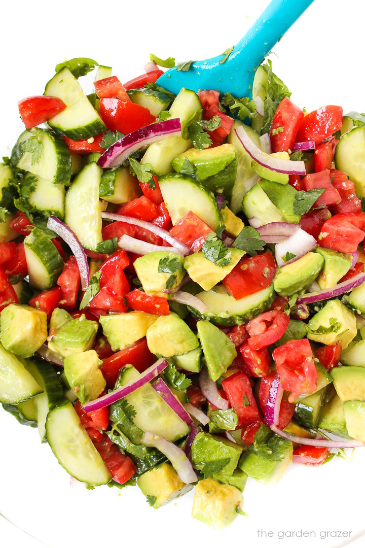 Fresh salad mixed together in a large glass bowl with blue spatula