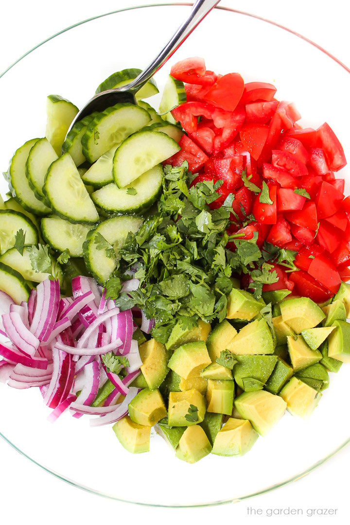 Overhead view of cucumber tomato avocado salad ingredients in a large bowl before stirring together