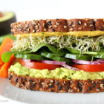 Avocado Sandwich on a plate with tomato, spinach, sprouts, and onion