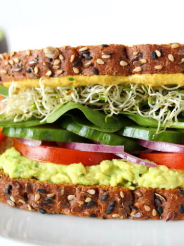 Avocado Sandwich on a plate with tomato, spinach, sprouts, and onion