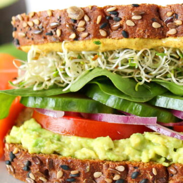 Vegan avocado sandwich with veggies and sprouts on a white plate