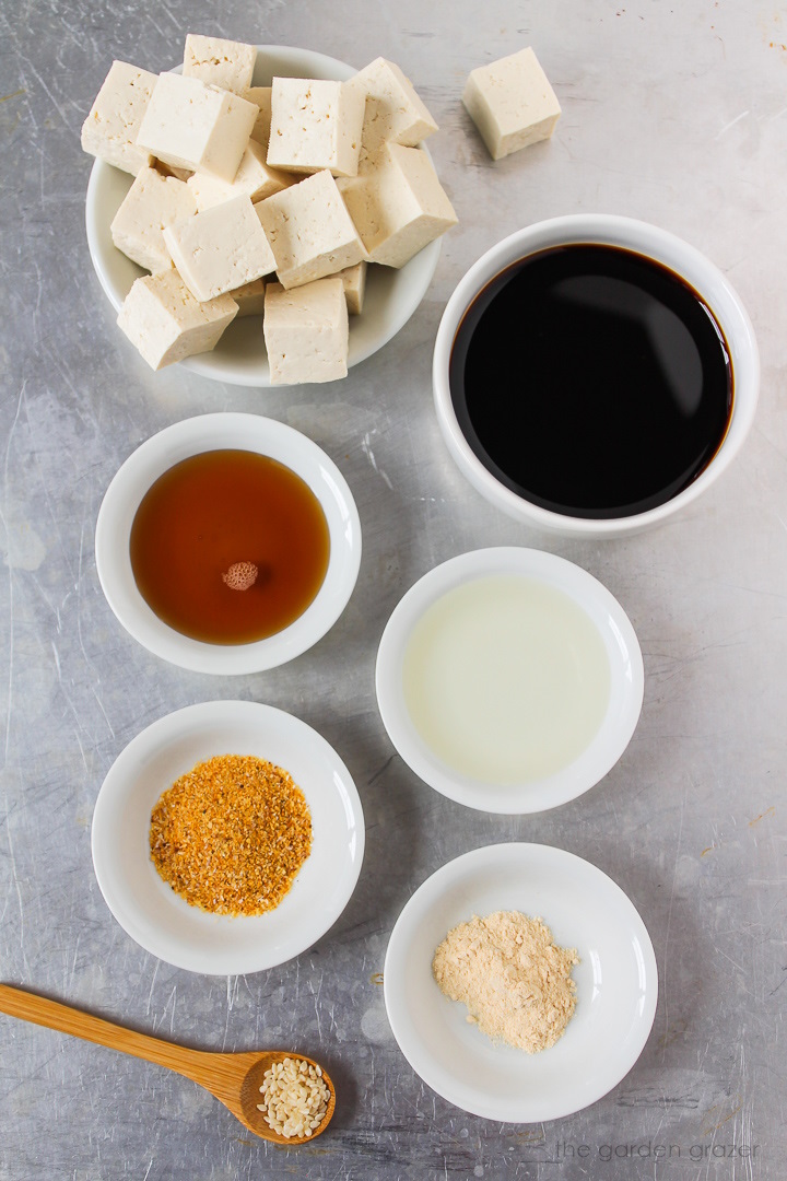 Overhead view of tamari, maple syrup, rice vinegar, sesame seeds, and seasoning ingredients laid out on a metal tray