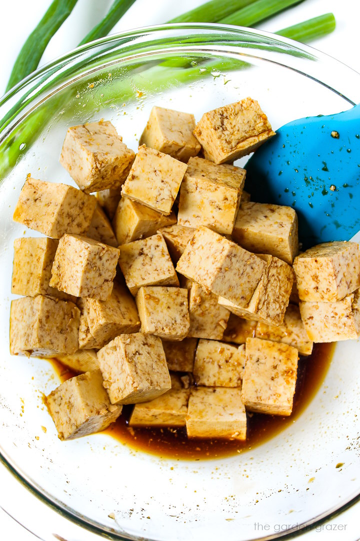 Preparing tofu cubes with a savory marinade in a large glass bowl before baking