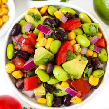 Avocado edamame salad with black beans and tomatoes in a small white bowl