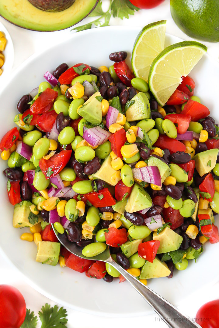 Black bean edamame avocado salad with cilantro lime dressing in a large white bowl with lime slices