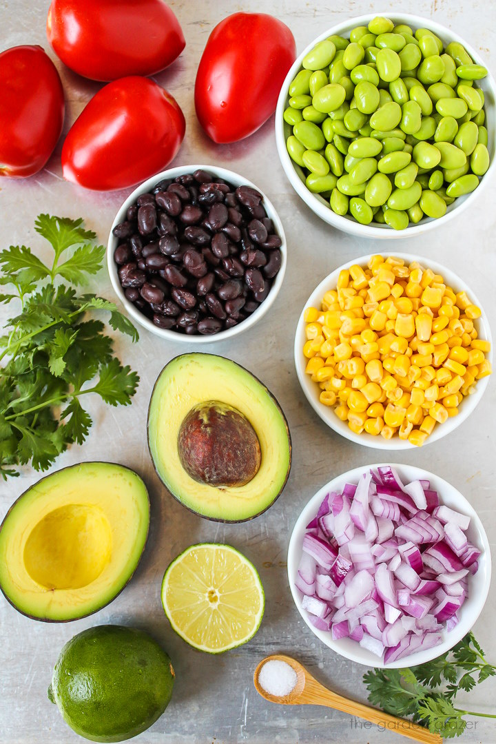 Edamame, tomatoes, sweet corn, onion, lime, salt, and fresh cilantro ingredients laid out on a metal tray