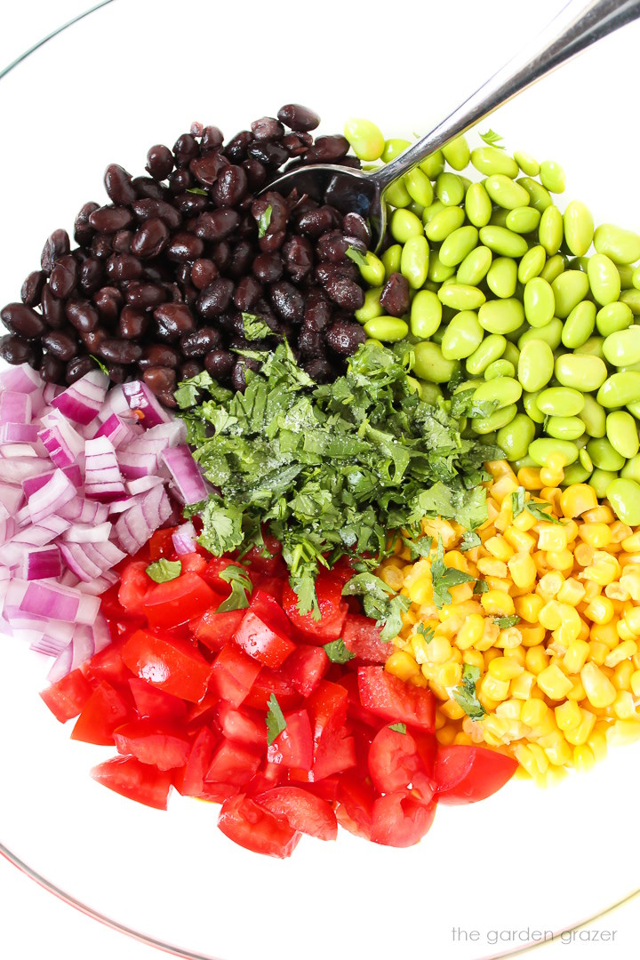 Overhead view of preparing avocado edamame salad in a large glass bowl before mixing together