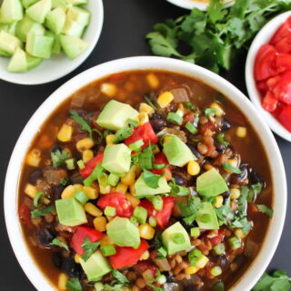 Bowl of black bean lentil taco soup with avocado, corn, and tomatoes