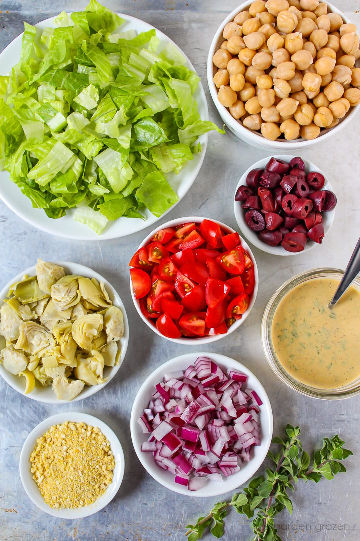 Romaine lettuce, garbanzo beans, tomato, olives, artichoke, and onion ingredients laid out on a metal tray