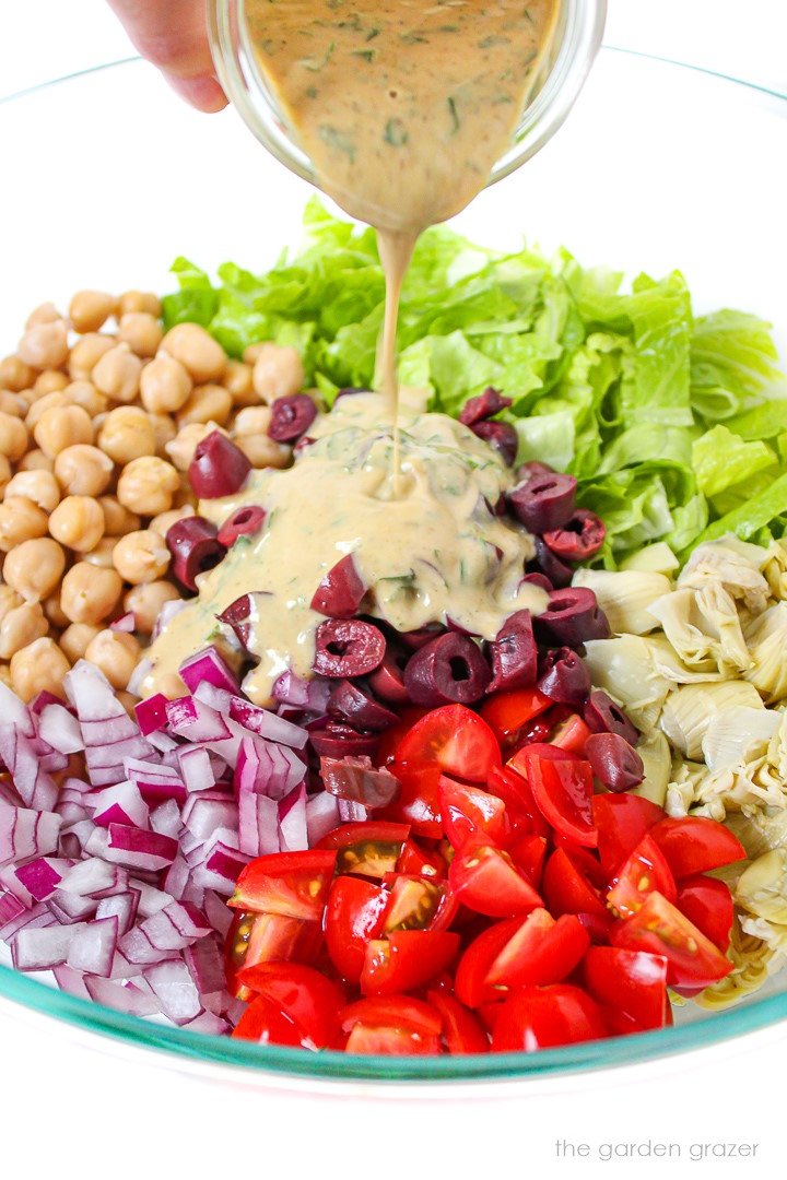 Dressing being poured on Italian salad ingredients in a large glass bowl