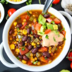 Vegan lentil taco soup with black beans in a white bowl topped with avocado and chipotle sauce
