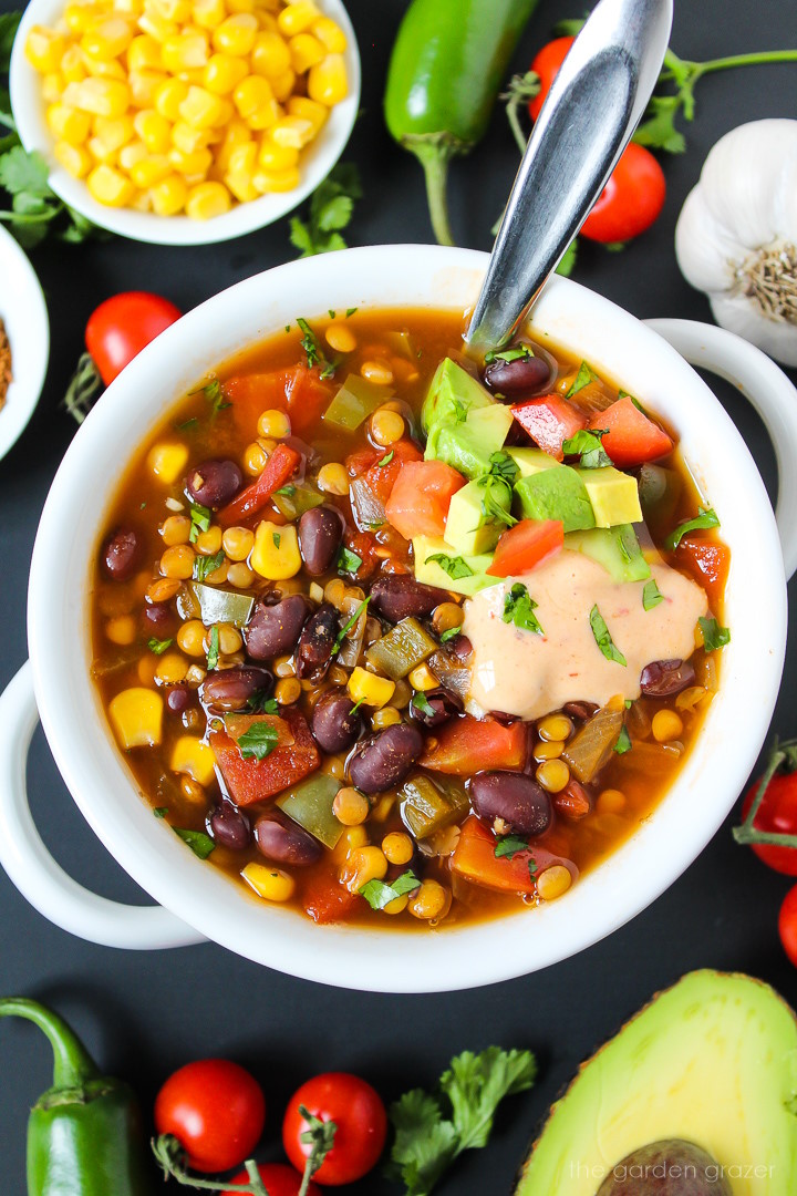 Vegan lentil taco soup with black beans in a white bowl topped with avocado and chipotle sauce