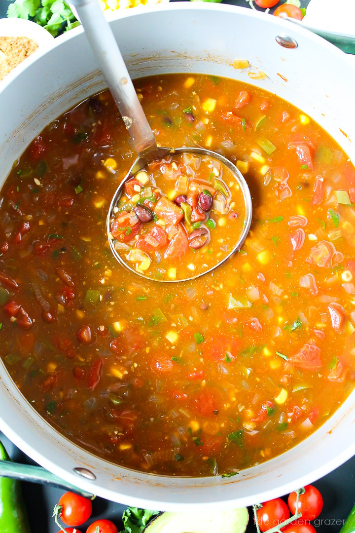 Ladle lifting up vegan lentil taco soup from a large pot during cooking