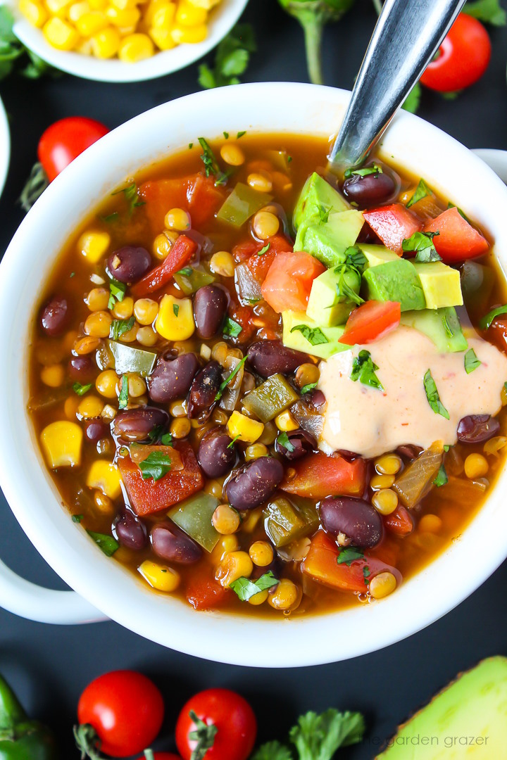 Close up view of vegan lentil black bean taco soup in a white serving bowl with spoon