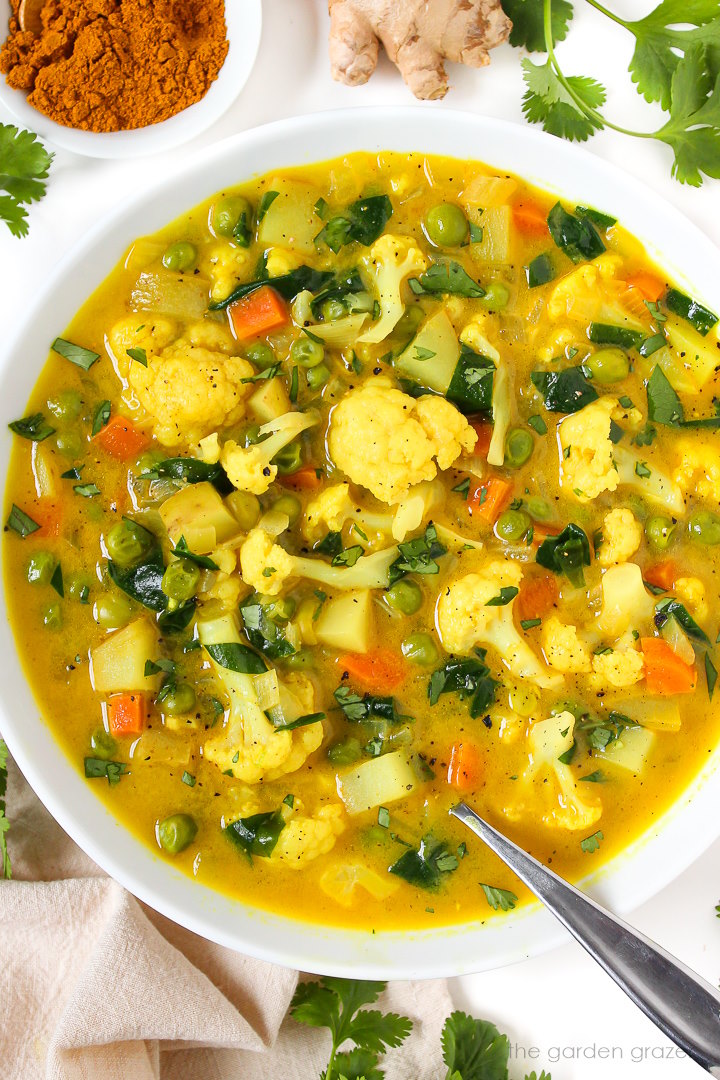 Close-up view of coconut curry vegetable soup in a white bowl with spoon