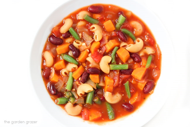 Bowl of soup with pasta, kidney beans, and vegetables in a white bowl with spoon
