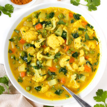 Overhead view of vegan coconut curry vegetable soup in a white bowl garnished with fresh cilantro