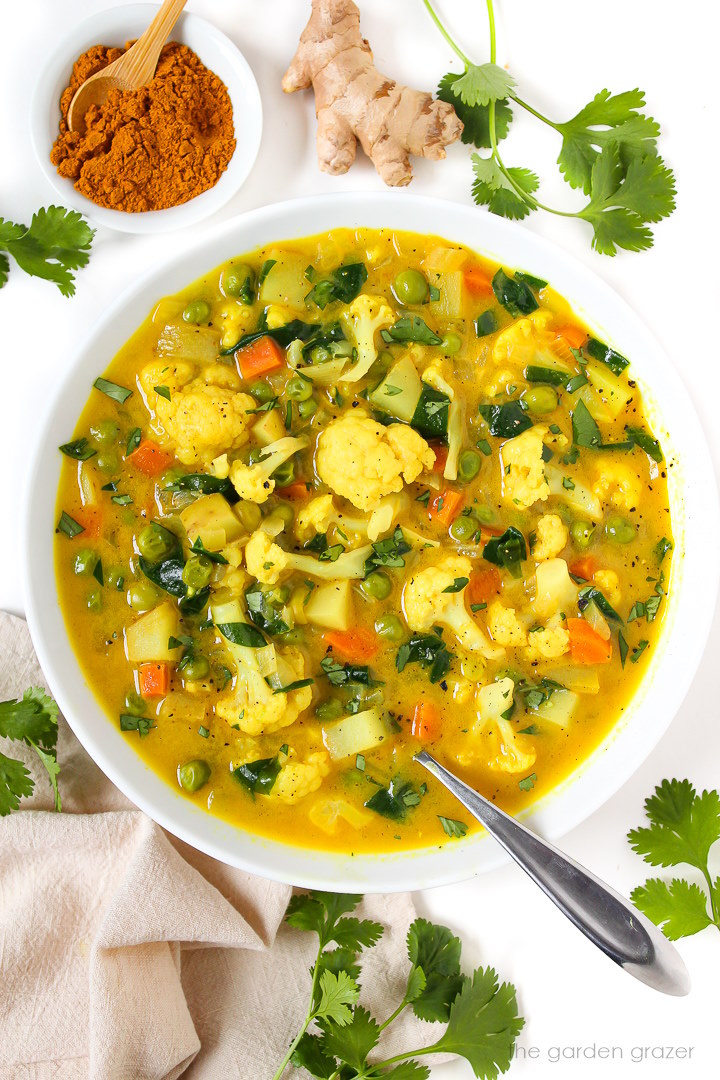 Overhead view of vegan coconut curry vegetable soup in a white bowl garnished with fresh cilantro