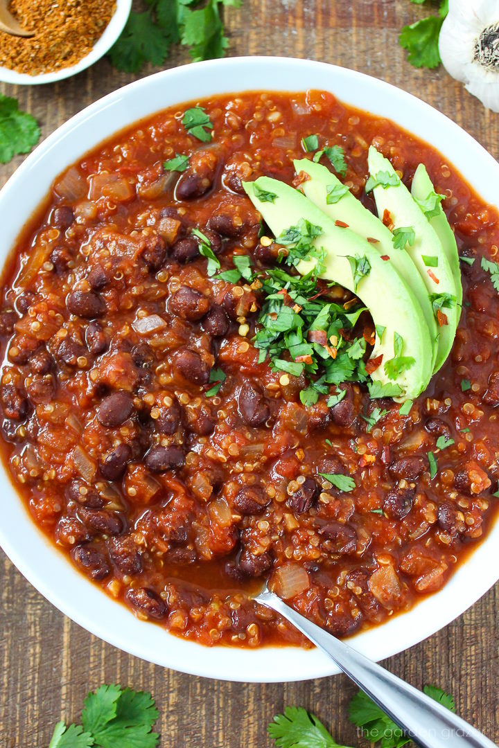Close up view of smoky black bean quinoa chili in a white serving bowl topped with avocado and cilantro