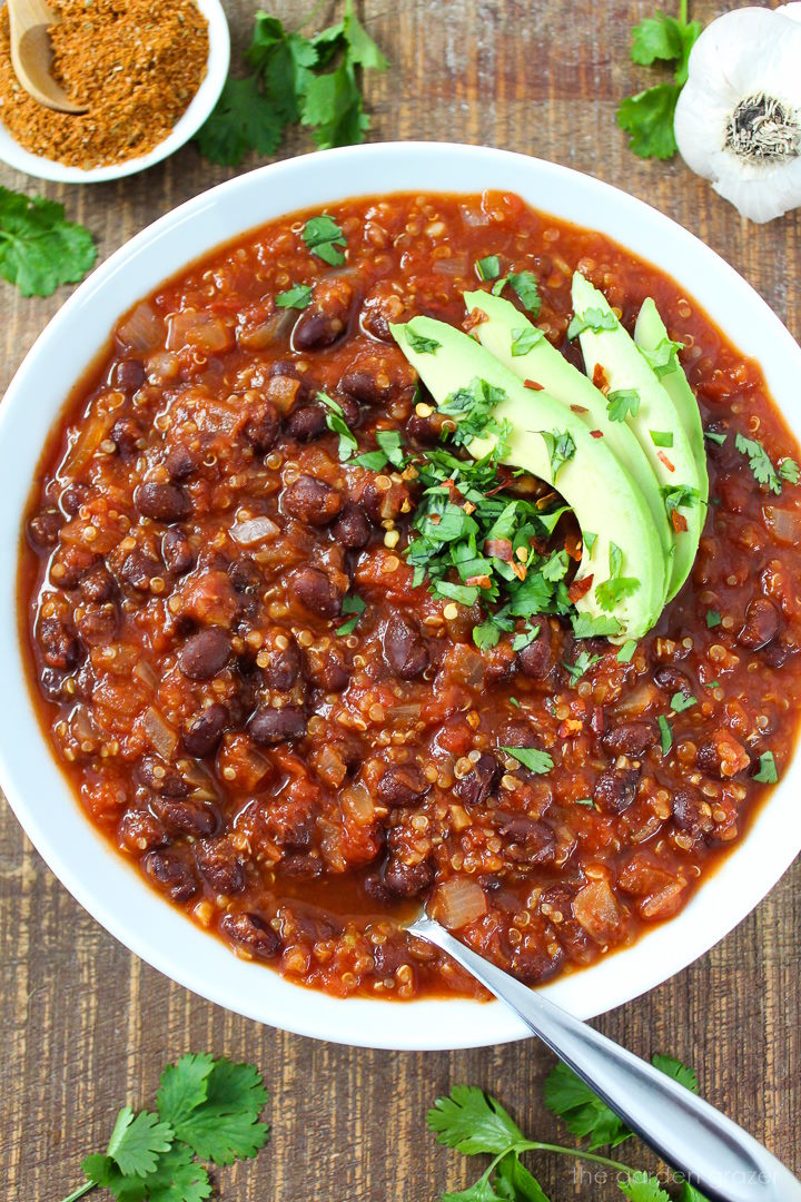 Smoky chipotle black bean quinoa chili in a white bowl with avocado and serving spoon