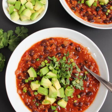 Bowls of smoky chipotle black bean chili with spoon and fresh avocado