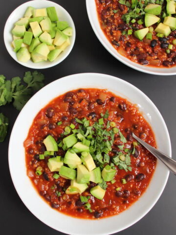Bowls of smoky chipotle black bean chili with spoon and fresh avocado