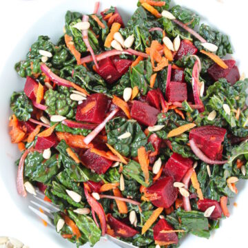 Roasted beet and kale salad on a white plate with serving fork