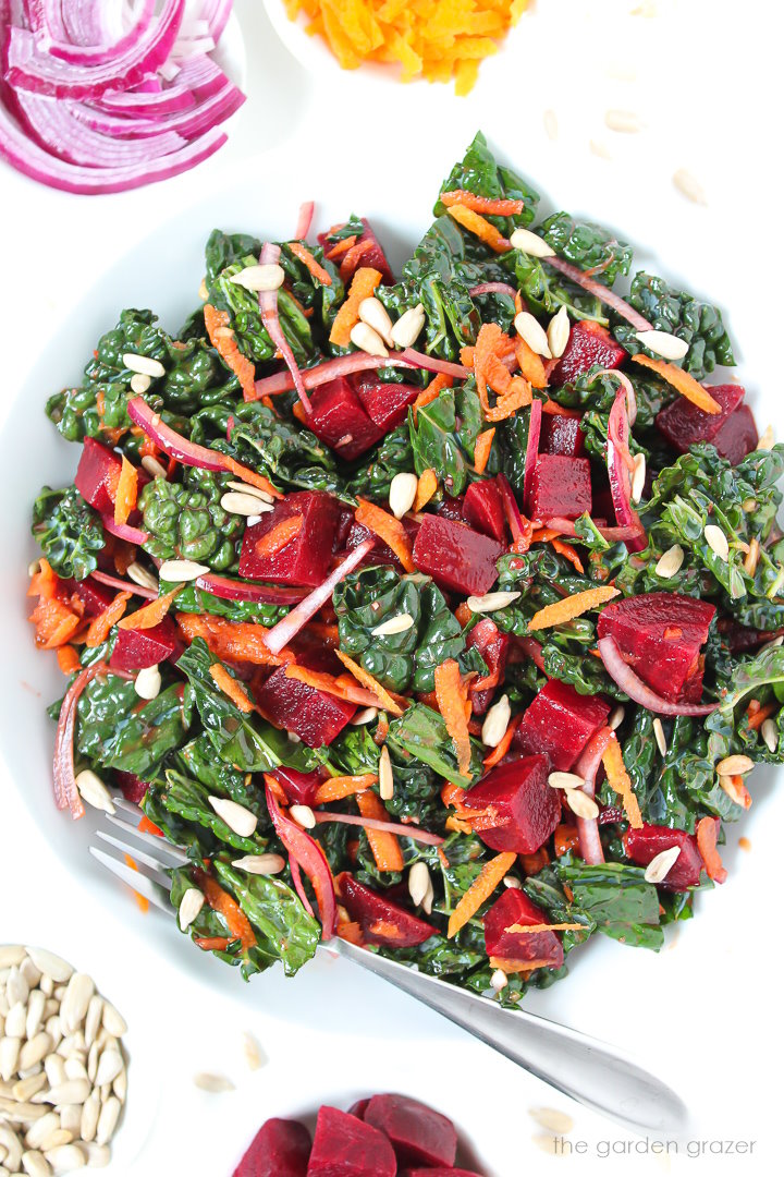 Roasted beet and kale salad on a white plate with serving fork