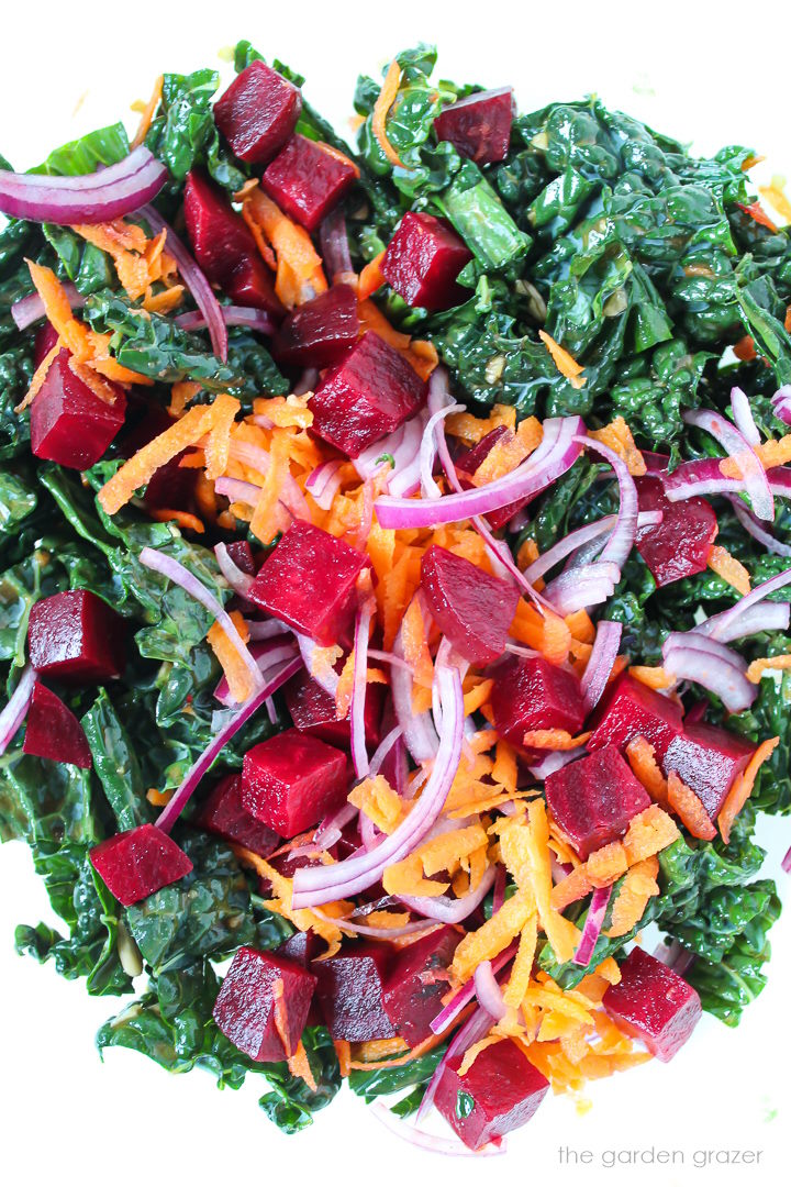 Mixing together ingredients for kale beet salad in a large glass bowl