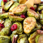 Close up view of maple balsamic Brussels sprouts in a white serving bowl with cranberries and pecans