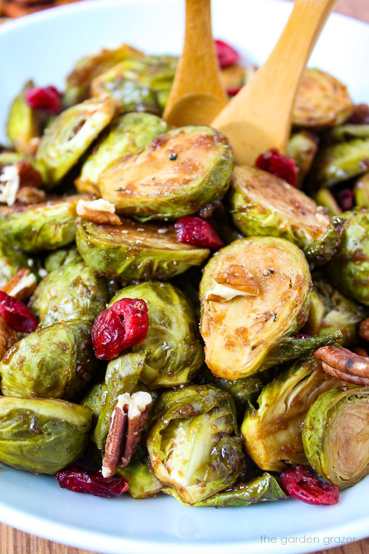 Close up view of maple balsamic Brussels sprouts in a white serving bowl with cranberries and pecans