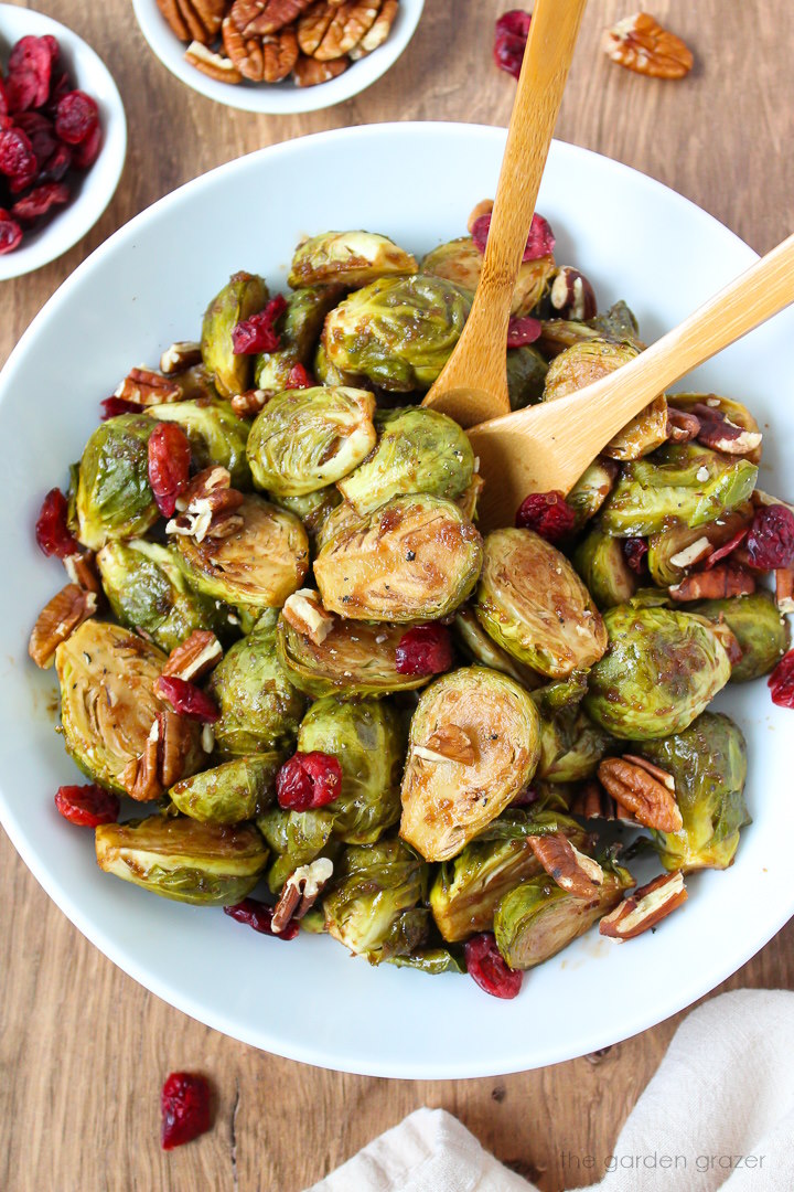 Roasted maple balsamic Brussels sprouts in a white serving bowl garnished with pecans and dried cranberries