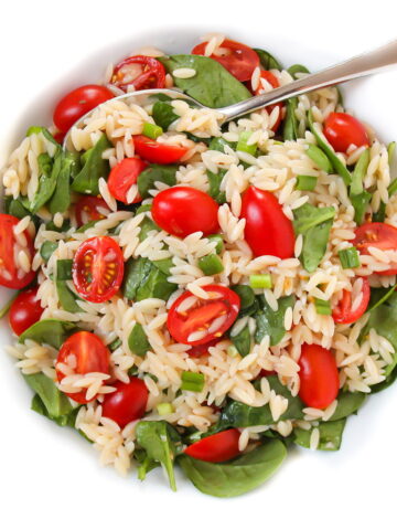 Orzo spinach salad in a white bowl with spoon