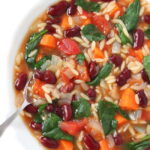 Bowl of kidney bean, orzo, spinach soup with a spoon