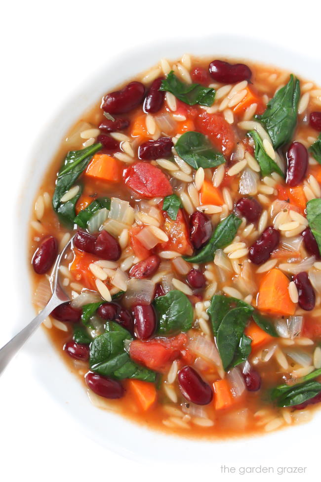 Bowl of kidney bean, orzo, spinach soup with a spoon