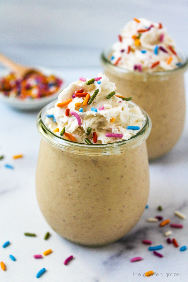 Vegan birthday cake batter shake served in small glass jars topped with whipped cream and rainbow sprinkles