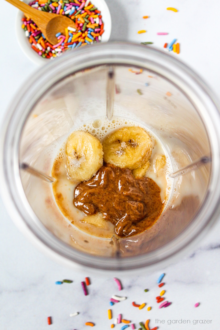 Overhead view of preparing vegan birthday cake batter shake ingredients in a blender cup before blending